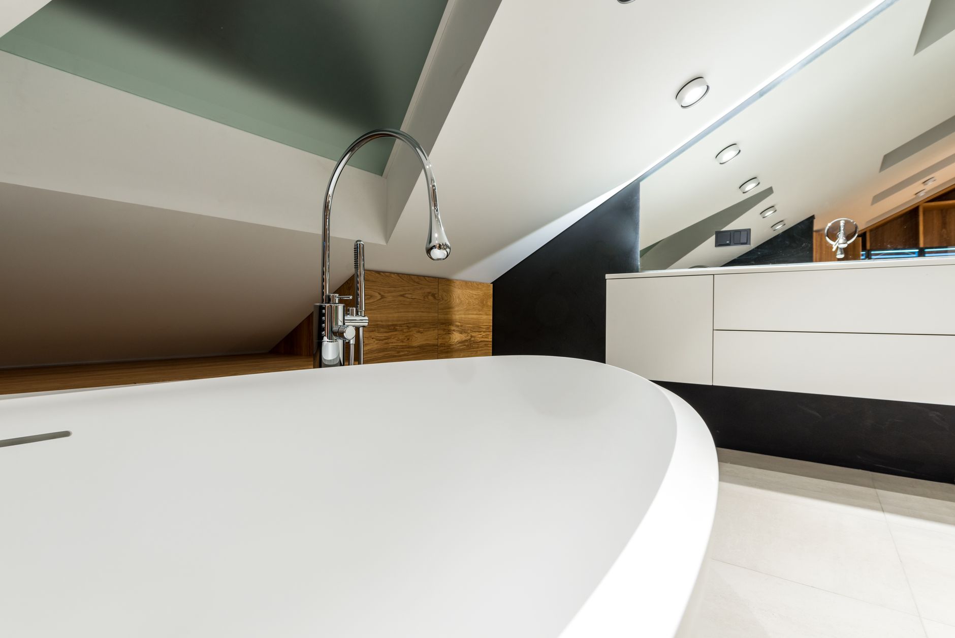 Interior of stylish bathroom with rounded bathtub under glass window in mansard of cottage
