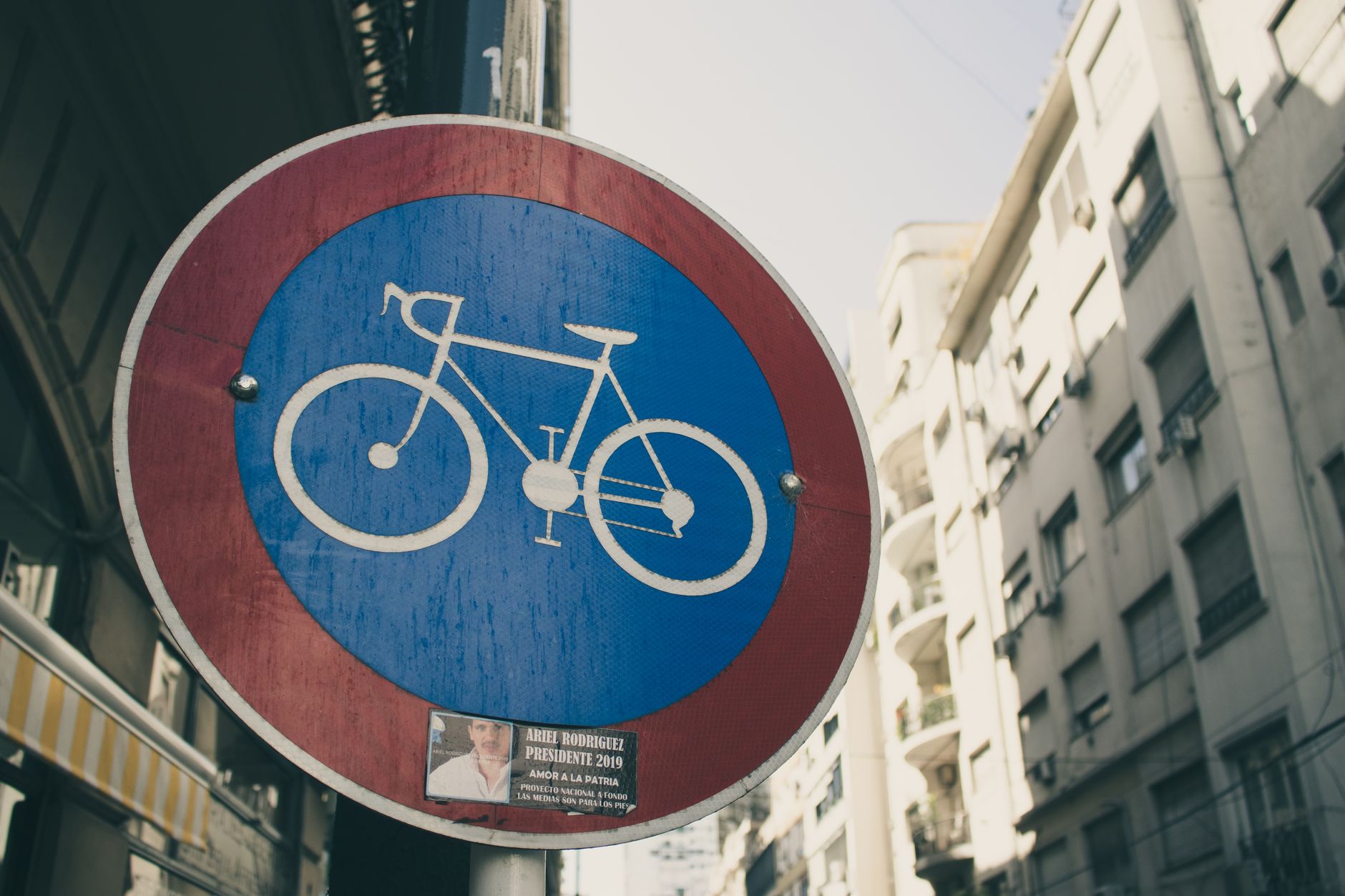 A bicycle lane sign against a city street background during the day.